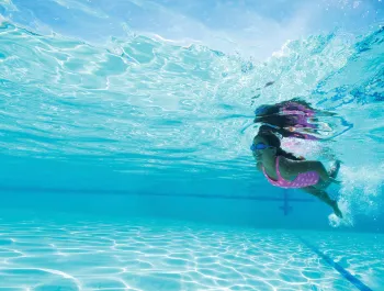 A photo of a girl with goggles swimming underwater.